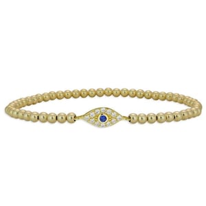 May include: A gold beaded bracelet with a small evil eye charm. The charm is set with clear and blue stones.
