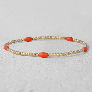 May include: A gold bracelet with small, round beads and four larger, oval-shaped red beads.