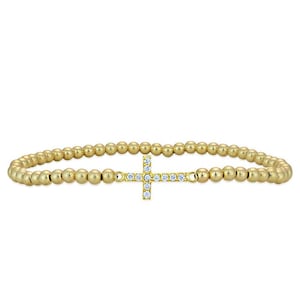 May include: A gold beaded bracelet with a small, clear crystal cross charm.