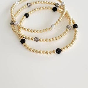 May include: Three gold beaded bracelets with black and white sparkly beads.