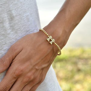 May include: A gold beaded bracelet with a charm of two figures holding hands, both figures are encrusted with small clear stones.