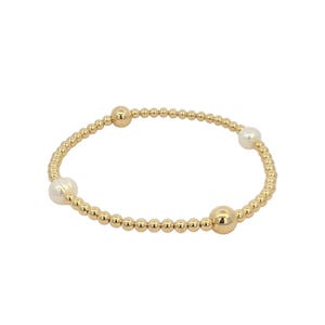 May include: A gold beaded bracelet with three white pearls.