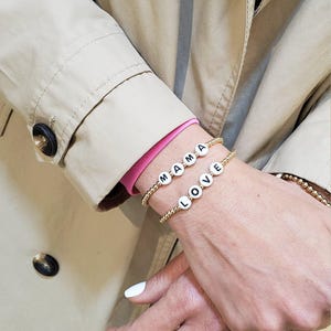 May include: Two gold beaded bracelets with white letter beads spelling out "MAMA" and "LOVE".