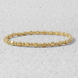May include: A gold beaded bracelet with small, square-shaped beads.