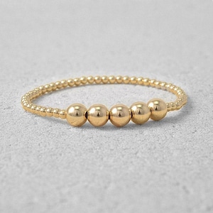 May include: A gold beaded bracelet with five round beads.