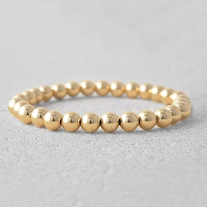 May include: A gold beaded bracelet with a simple design. The bracelet is made of small, round beads that are evenly spaced.