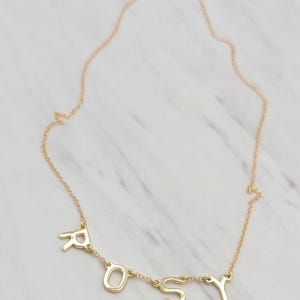 May include: A gold chain necklace with the word "ROSY" spelled out in individual letters.
