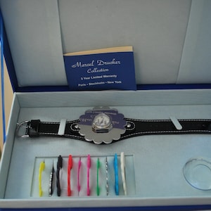 May include: A silver watch with a flower-shaped face and a black leather band. The watch is in a blue box with a white interior. The box also contains a small clear plastic container and a set of colorful tools.