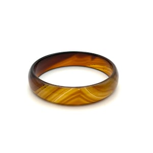 May include: A smooth, circular bangle bracelet crafted from polished agate stone. The piece features a translucent, banded pattern with rich, warm color gradients transitioning from deep chocolate brown to golden amber and creamy yellow tones.