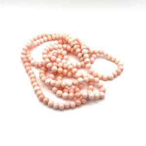 May include: A strand of light pink coral beads, each with a smooth, round shape. The beads are strung together, creating a necklace or bracelet. The coral has a natural, organic appearance, with variations in color and texture.