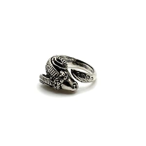 May include: A silver-colored ring featuring a ram's head design. The ram's head is detailed with textured fur and horns. The ring band has a swirling pattern on the end. The ring is set against a white background.