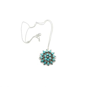 May include: A silver necklace featuring a pendant with a sunburst design. The pendant is adorned with turquoise teardrop-shaped stones and a central cluster of smaller turquoise stones. The necklace is displayed on a white background.