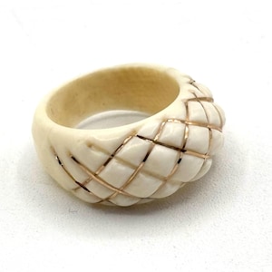 May include: A white ring with a carved design and gold accents. The ring is made of bone and has a wide band.