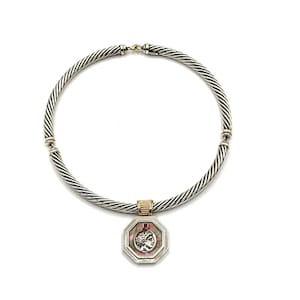 May include: Silver-tone necklace with a twisted cable design. The necklace features a gold-tone clasp and a pendant with a pink background and a profile of a person. The pendant is octagonal and has a silver-tone border.