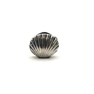May include: A polished silver-toned metal object shaped like a scallop shell. The surface features deep, radiating vertical ridges that create a fan-like pattern. The metallic finish reflects light, highlighting the curved, semi-circular form.