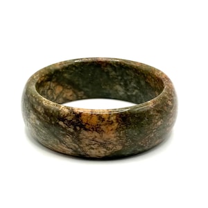 May include: A polished bangle bracelet crafted from a solid piece of stone, featuring a mottled pattern of deep forest green, earthy brown, and tan hues. The circular accessory has a smooth, rounded exterior surface and a consistent thickness.