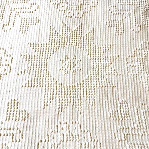 May include: A cream-colored textile featuring a repeating embossed pattern of suns and hearts. The fabric has a vertical ribbed texture with raised, dot-like stitches forming the shapes. The design is consistent across the entire surface area.