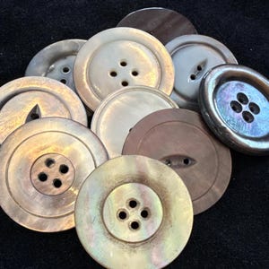 May include: A collection of iridescent buttons in various sizes and shades of cream, brown, and gray. The buttons have either four or two holes, and some feature a subtle, pearlescent sheen. These buttons are ideal for sewing and craft projects.