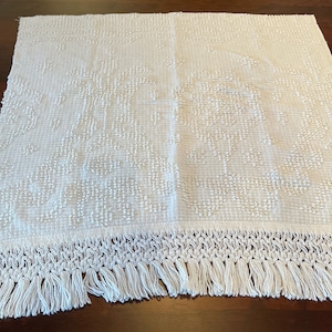 May include: White crocheted throw blanket with a fringe border. The blanket has a textured design with raised dots.