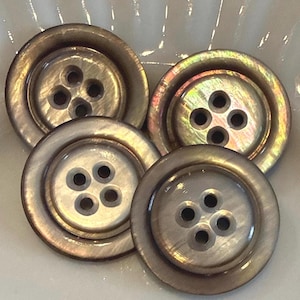 May include: Four iridescent, round buttons with four holes each. The buttons have a pearlescent sheen with a dark rim. The buttons are a neutral color, with hints of gold and green.