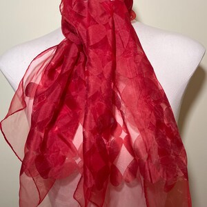 May include: A red sheer scarf with a heart pattern. The scarf is draped over a mannequin's neck.