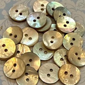 May include: A collection of round, iridescent buttons in various sizes. The buttons have two or four holes and a pearlescent sheen, with colors ranging from gold to cream. These decorative buttons are ideal for sewing and craft projects.