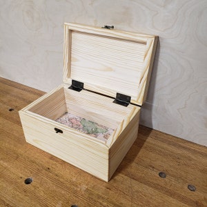 May include: A wooden box with a hinged lid and a map-like design on the inside. The box is made of light wood and has a natural finish.
