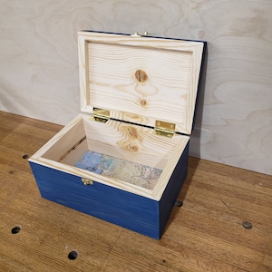 May include: A blue wooden box with a hinged lid and brass hinges. The box is open and the inside is lined with a patterned paper.