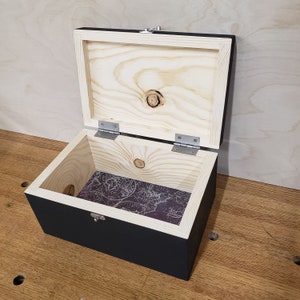 May include: A black wooden box with a hinged lid. The inside of the box is lined with a patterned paper featuring a world map.
