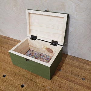 May include: A green wooden box with a hinged lid and a brass latch. The box is open and the inside is lined with a patterned paper.