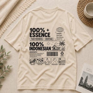 Könnte beinhalten: Ein beiges Kurzarm-T-Shirt mit schwarzem Grafiktext und Illustrationen auf der Rückseite. Das Design enthält die Wörter 100% ESSENCE und 100% INDONESIAN, einen Strichcode, einen Globus, ein Haus, eine Palme und Symbole für Essen und Familie.