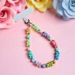 Puede incluir: Un colorido dije para teléfono con un diseño de cuentas con forma de ositos de goma en varios colores pastel. El dije incluye una etiqueta blanca para sujetar al teléfono y está adornado con cuentas de color plateado.