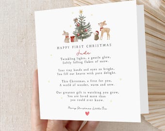 May include: A white Christmas card with the text "Happy First Christmas" and a poem. The card features a watercolor illustration of a Christmas tree, gifts, and woodland animals. The name "Jude" is written in cursive.