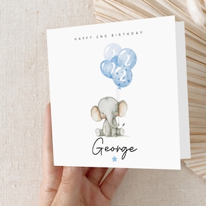 May include: A white card with blue and white balloons and a gray elephant holding a blue balloon. The card says "Happy 2nd Birthday George" with a blue star.