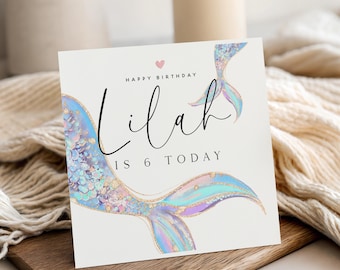 May include: A square birthday greeting card with a white background featuring a colourful mermaid tail illustration in shades of blue, purple, and gold. The text reads "HAPPY BIRTHDAY Lilah IS 6 TODAY" with a small pink heart above the name.