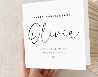 May include: White card with black text that reads "Happy Anniversary Olivia First Year Down Forever To Go" with a pink heart symbol.