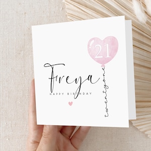 May include: A white birthday card with the name "Freya" in elegant script. A pink heart-shaped balloon with the number "21" is featured. The words "Happy Birthday" and "twentyone" are also present.