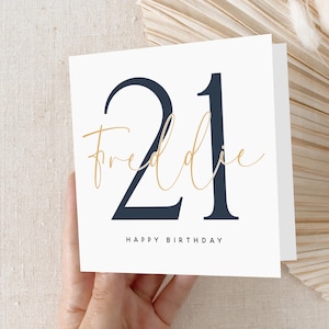 May include: A white card with a navy blue number "21" and the text "Freddie" in gold script. The card also says "Happy Birthday".
