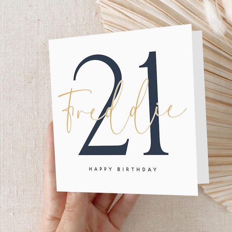 May include: A white card with a navy blue number "21" and the text "Freddie" in gold script. The card also says "Happy Birthday".