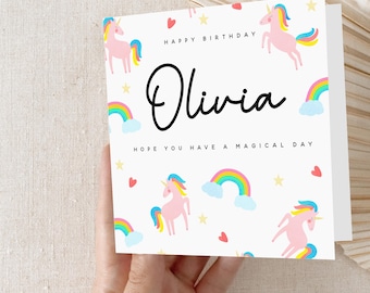 May include: A white card with a pink unicorn, rainbow, and stars pattern. The card says "Happy Birthday Olivia Hope you have a magical day".