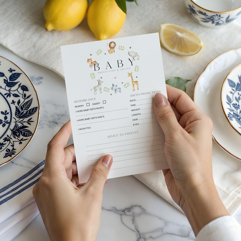 May include: A white baby shower prediction and advice card held by hands. The card features the word "BABY" with animal illustrations and sections for resemblance, birth predictions, and advice to parents.