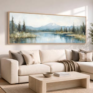 Puede incluir: Una pintura de paisaje panorámico en un marco de madera clara que muestra un pico de montaña nevado sobre un lago tranquilo. La escena incluye pinos de color verde oscuro a lo largo de la orilla con tonos azules y blancos reflejados en el agua.