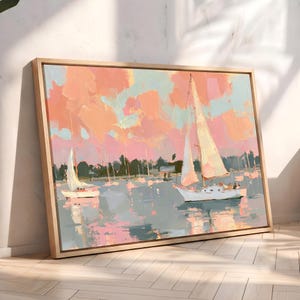 May include: A framed canvas painting depicting two sailboats on calm water under a sky filled with soft peach, pink, and light blue clouds. The scene features a dark treeline in the distance, with the boats reflected in the water below.