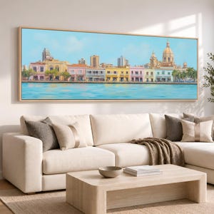 May include: A panoramic landscape painting in a light wood frame depicting a coastal city skyline with colorful buildings, a prominent domed cathedral, and palm trees along a waterfront, all set against a clear, bright blue sky and water.