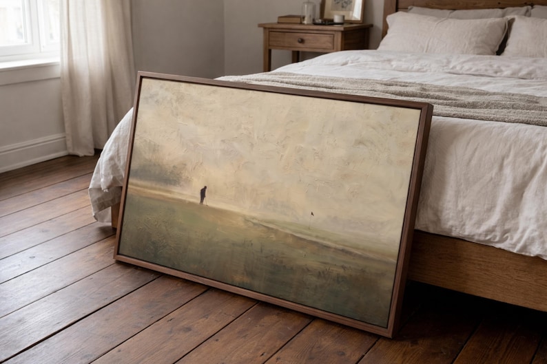 Puede incluir: Una pieza de arte mural rectangular enmarcada que presenta una pintura de paisaje con una paleta de colores apagados en beige, bronceado y verde oliva. La obra muestra un campo vasto y brumoso bajo un cielo nublado con una figura solitaria.
