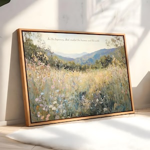 May include: A framed landscape painting depicting a field of wildflowers and tall grass with a mountain range in the background. The artwork is in a wooden frame and features the text "In the beginning, God created the heavens and the earth."