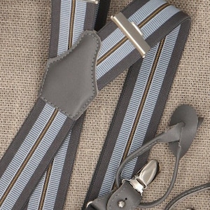 May include: Gray suspenders with blue and brown stripes. The suspenders have leather accents and metal clips.