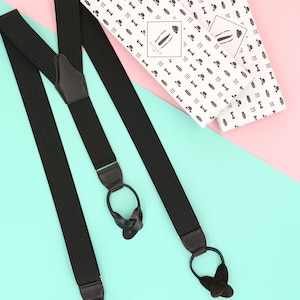 Peut inclure: Bretelles noires avec des détails en cuir et un design distinctif. Les bretelles sont présentées avec deux boîtes avec un motif répété de nœuds papillon et de chapeaux. Les boîtes portent l'inscription "RANGER".