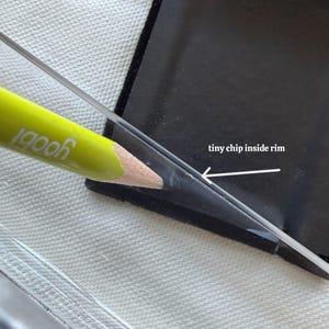 May include: Close-up of a black, rectangular object with a clear, angled edge. A yellow pencil with the word "yoobi" is pointing at a small chip inside the rim. The text "tiny chip inside rim" is also visible.