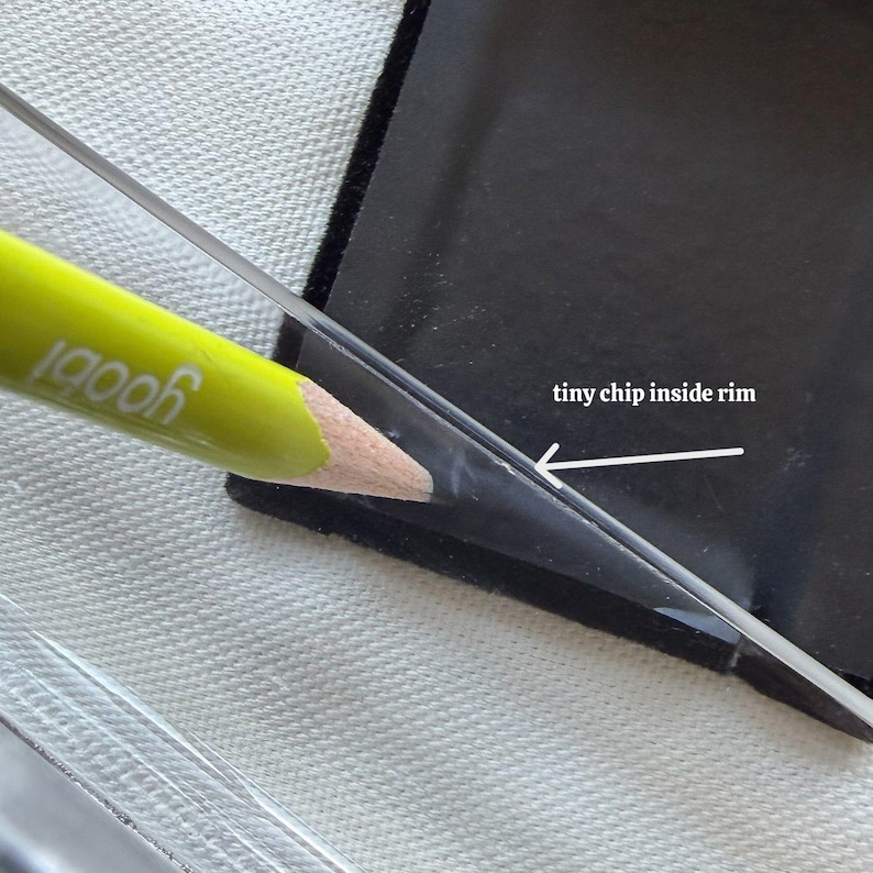 May include: Close-up of a black, rectangular object with a clear, angled edge. A yellow pencil with the word "yoobi" is pointing at a small chip inside the rim. The text "tiny chip inside rim" is also visible.